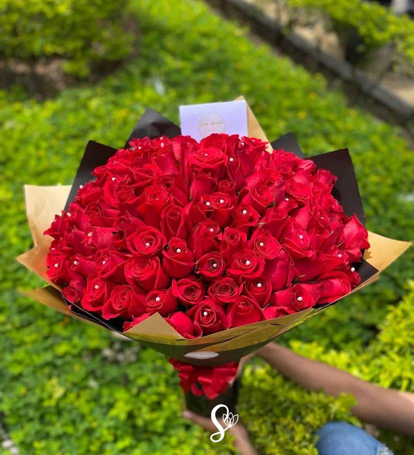 "Impresionante arreglo floral de 100 rosas rojas frescas de tallo largo dispuestas de forma circular y compacta."